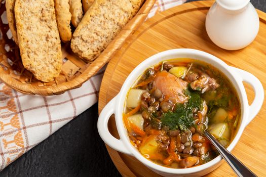 Lentil soup with chicken in a white bowl on a wooden board on a black table, top view.