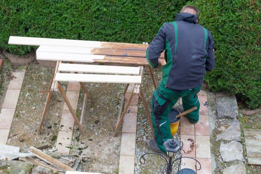 A man holds a paintbrush in hand and strokes paint color on wooden furniture. Concept renovation garden furniture.