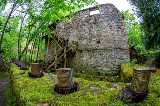 Old water mill and rusted barrels in the beautiful forest park in Latvia. Moss covered ancient mill in old park. Shot with fisheye lens. 
