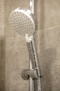 Fresh shower behind wet glass window with water drops splashing. Modern bathroom