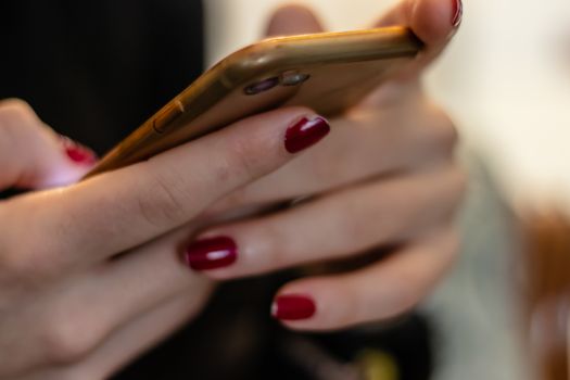 a girl using her smartphone with blurry background and red nail polish. a good looking shoot.