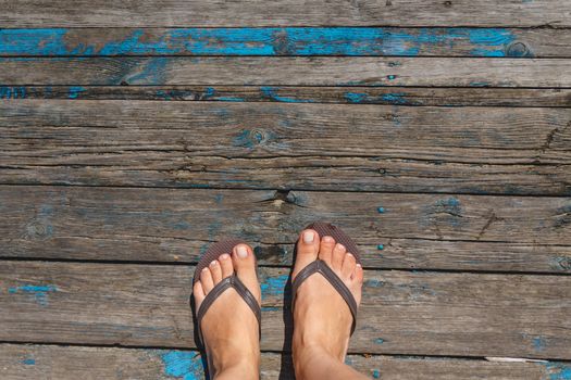 Top view, photo of female legs in beach flip flops on a wooden old floor. Photos on vacation, beach, summer.