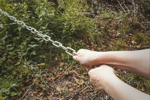 Female hands pulling a thick metal chain - the concept of hard work, unbearable burden.