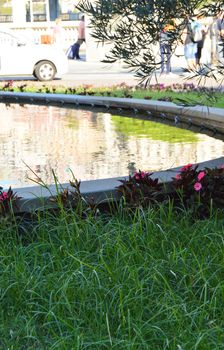 Vertical shot of a part of the fountain with a lawn and a pond in front of the sea station in Genoa.