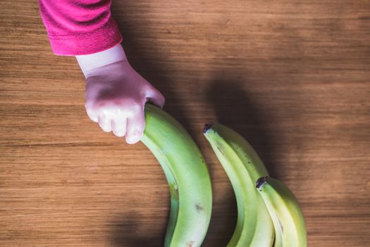 Three bananas and a babys hand forming a curved line on a wooden table