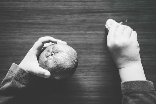 Black and white picture showing the hands of a kid, one grabbing a tangerine and the other grabbing a slice.