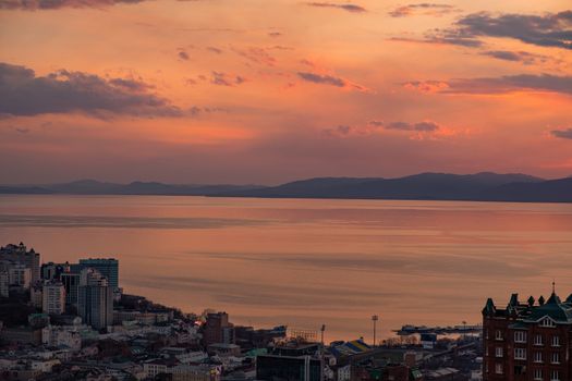 View of the city of Vladivostok from the hill eagle's nest . Sunset. The sky is orange and pink. Sea and city at sunset.