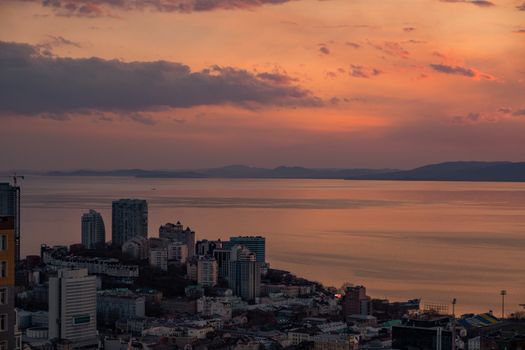 View of the city of Vladivostok from the hill eagle's nest . Sunset. The sky is orange and pink. Sea and city at sunset.