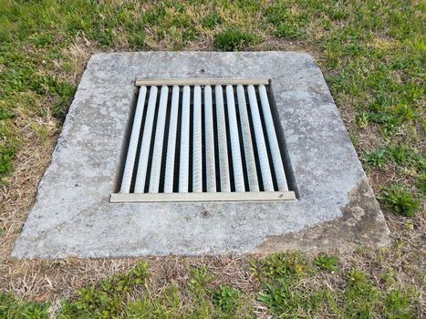 iron metal grate and cement drain and green grass or lawn