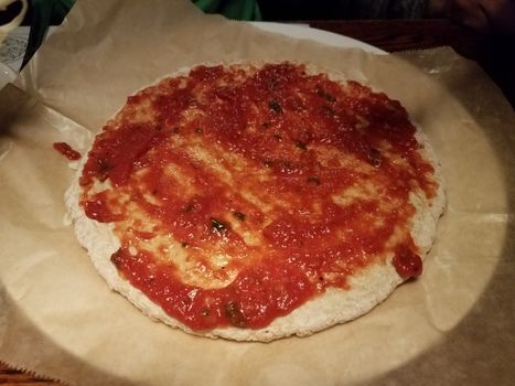 pizza dough and red tomato sauce on wax paper