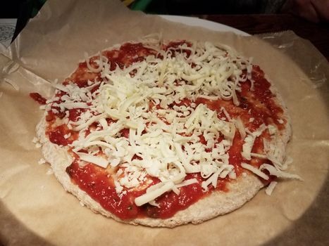 pizza dough and red tomato sauce and cheese on wax paper