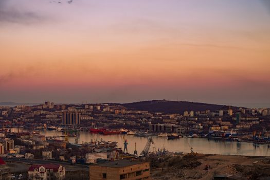 View of the city of Vladivostok from the hill eagle's nest . Sunset. The sky is orange and pink. Sea and city at sunset.