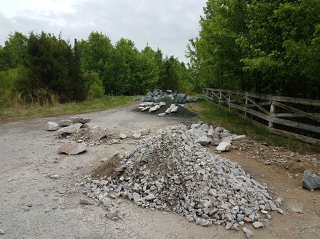 asphalt street or road with piles of grey rocks or stones and trees