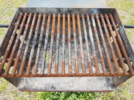 weathered and brown rusted metal bars on barbecue grill with soot and a hole