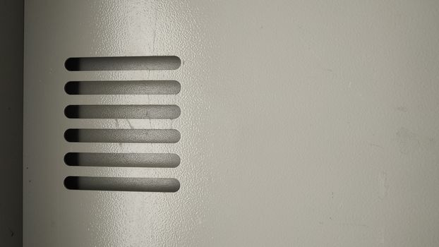 The ventilation grille in the metal wall is painted in a pale beige color.