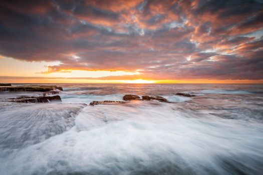 Tidal waves wash up onto the rocks and flow back to the ocean as cascading waterfalls.  Pretty sky overhead coloured by the rising sun