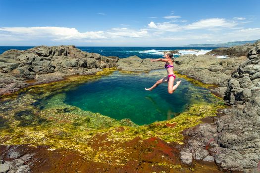 Woman in a mid air jump from the rocks into a beautiful clear blue rock pool on the coast of Australia