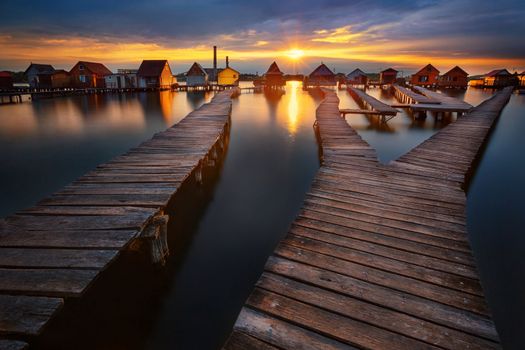 Sunset over lake Bokod with wooden pier and floating houses, power plant in background, Hungary