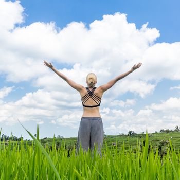 Relaxed healthy woman, arms rised, enjoying pure nature at beautiful green rice fields on Bali. Concept of healthy and clean environment, ecology, balance in life, freedom, happiness, and well being.
