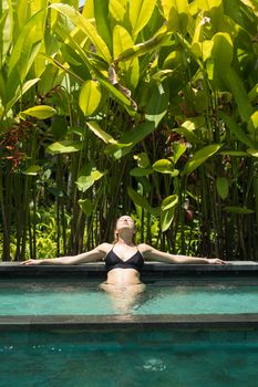 Sensual young woman relaxing in outdoor spa infinity swimming pool surrounded with lush tropical greenery of Ubud, Bali. Wellness, natural beauty and body care concept.