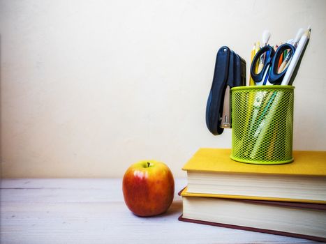 View on the pile of books, apple and cup with pencils lying on the wooden table