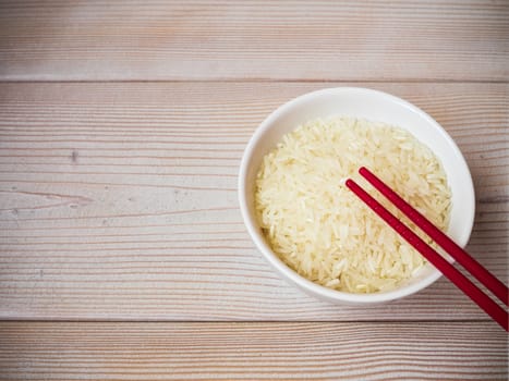 Ceramic bowl with uncooked rice and red chopsticks on the wooden table