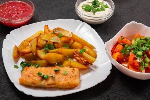 Fried fish and chips on a white plate on the kitchen table with tomato sauce, tartar sauce and pickled vegetables salad - photo, image.