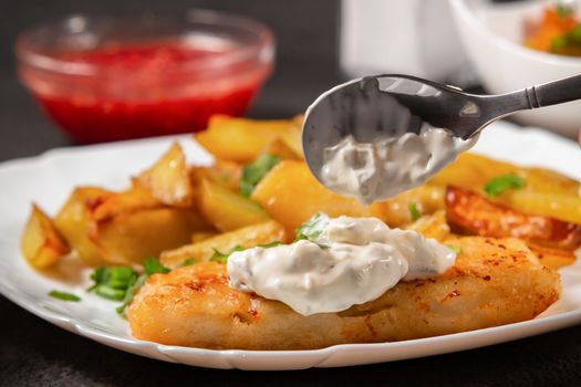 Fried fish and chips on a white plate on the kitchen table with tomato sauce, tartar sauce. Inpose on fish Tartar sauce - photo, image.