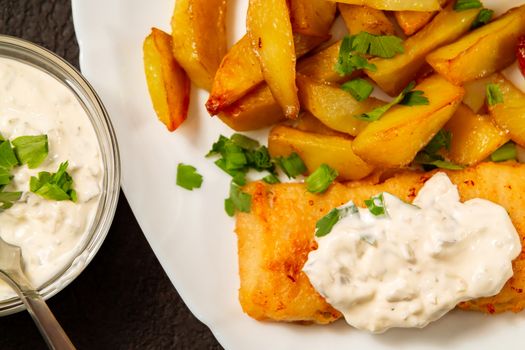 Fried fish and chips on a white plate on the kitchen table with tartar sauce close-up - photo, image.