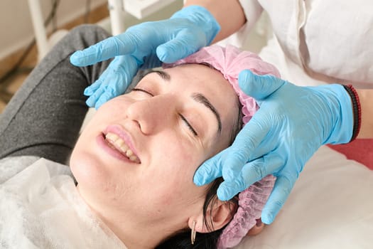 Young woman does professional facial massage after moisturizing, softening, regenerating, rejuvenating, toning cosmetic procedures in the beauty salon. Close-up view.