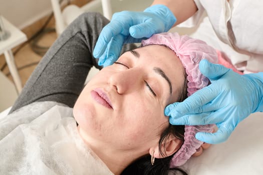 Young woman does professional facial massage after moisturizing, softening, regenerating, rejuvenating, toning cosmetic procedures in the beauty salon. Close-up view.