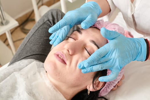 Young woman does professional facial massage after moisturizing, softening, regenerating, rejuvenating, toning cosmetic procedures in the beauty salon. Close-up view.