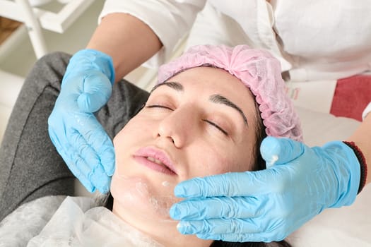 Young woman does professional facial massage after moisturizing, softening, regenerating, rejuvenating, toning cosmetic procedures in the beauty salon. Close-up view.