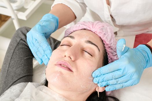 Young woman does professional facial massage after moisturizing, softening, regenerating, rejuvenating, toning cosmetic procedures in the beauty salon. Close-up view.