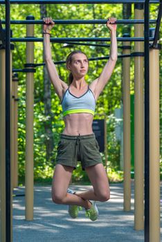 young and strong girl doing exercises on the press on the bar in the park