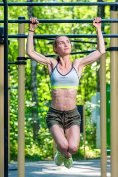 muscular strong woman on the crossbar is engaged in the park, press exercises