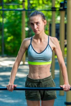 slim girl with a sports figure is engaged on the playground outside in the park