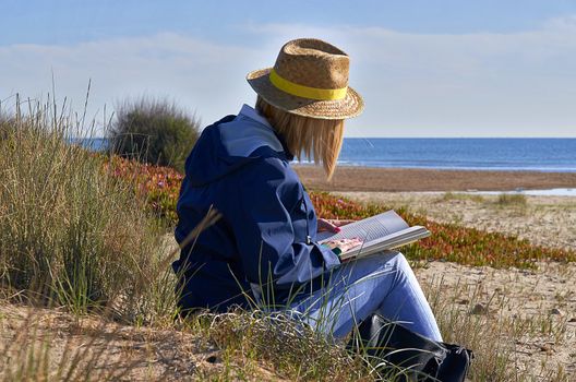 Woman sitting in the sun on the beach reading a book