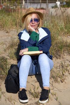 Woman sitting in the sun on the beach reading a book