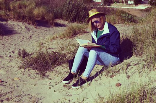 Woman sitting in the sun on the beach reading a book
