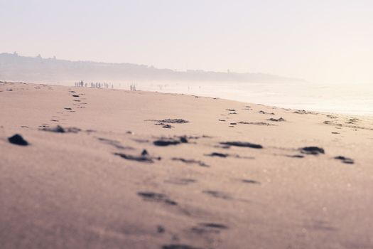 traces of people walking in the sand of the beach, the landscape is covered by fog