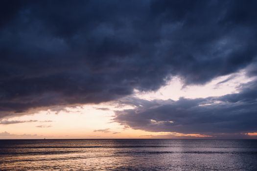 colorful sunset on the beach, the blue sky is covered in storm clouds and it is orange and yellow on the horizon