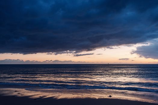 spectacular sunset on the beach, the blue sky is covered in storm clouds and it is orange and yellow on the horizon