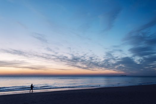 silhouette of a fisherman walking with his fishing rod by the seashore during a spectacular sunset in Chiclana, Cadiz, Andalusia, Spain