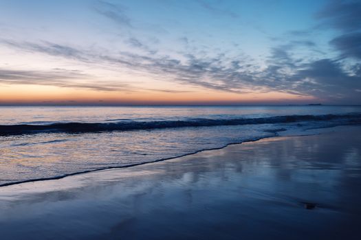 beautiful sunset on a lonely beach, the wet sand of the beach reflects the blue sky and the orange light of the horizon