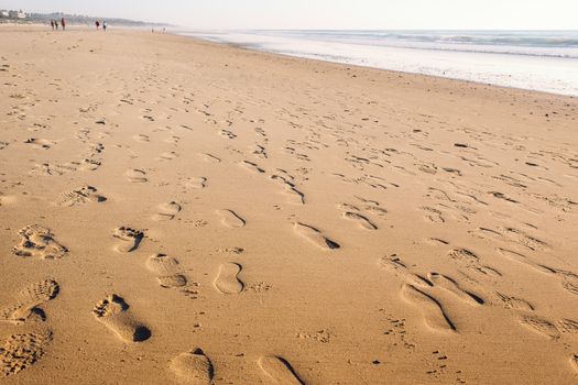 footprints in the wet sand of the beach, in the background there are people walking along the shore