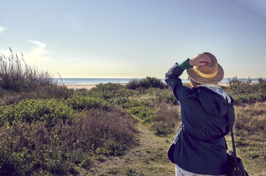 Woman with hat looking at the sea while walking