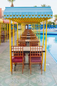 Outdoor wooden restaurant terrace with tables with four seats with a small roof against the sun.