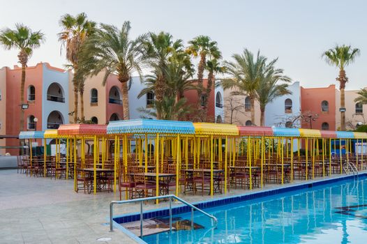 Outdoor wooden restaurant terrace with four-seater tables with a small roof against the sun along the pool