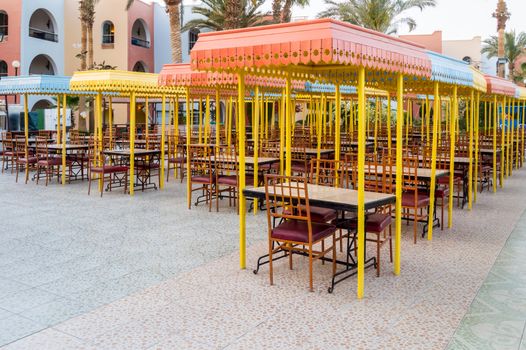 Outdoor wooden restaurant terrace with tables with four seats with a small roof against the sun.